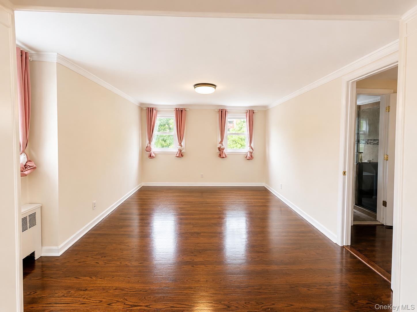 Polished wood-finish flooring, crown molding, and two windows with light-filtering treatments