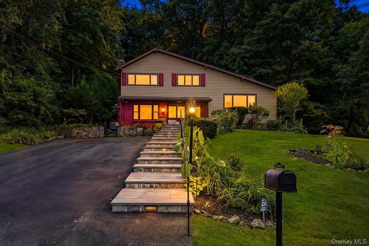 Split-level residence featuring a paved driveway, stone retaining walls, and a multi-level stone walkway.