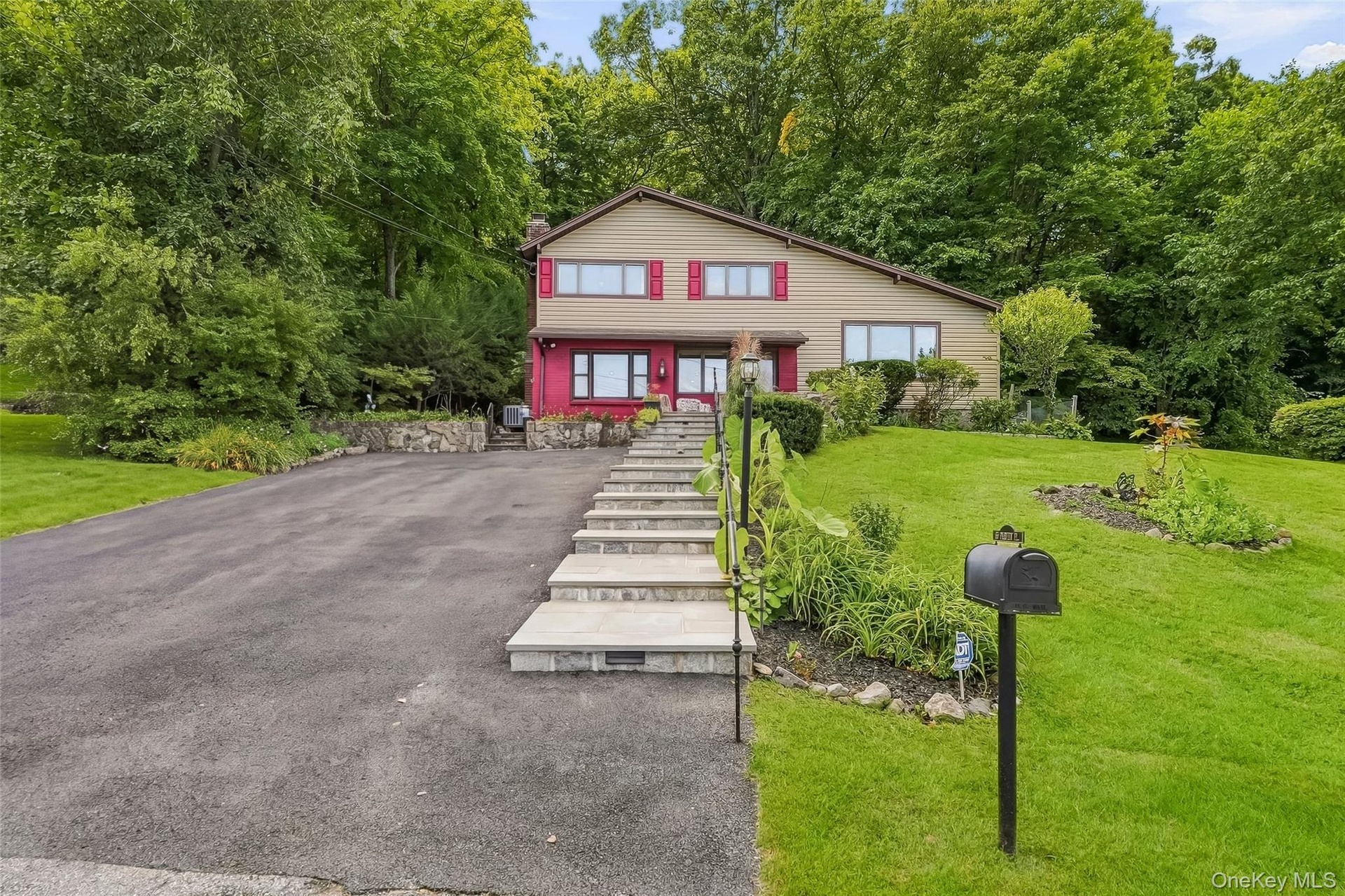 Split-level residence featuring a paved driveway, stone retaining walls, and a tiered stone walkway