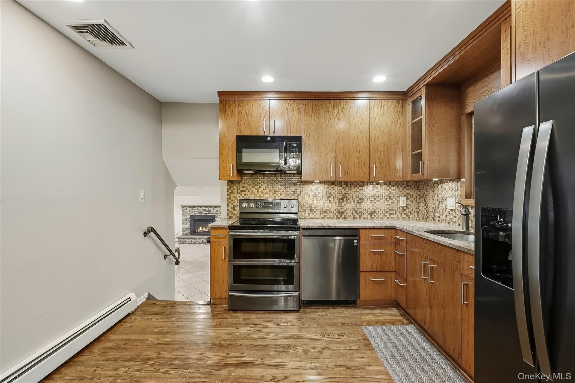 Kitchen with wood flooring featuring custom cabinetry, stainless steel appliances, and a tiled backsplash