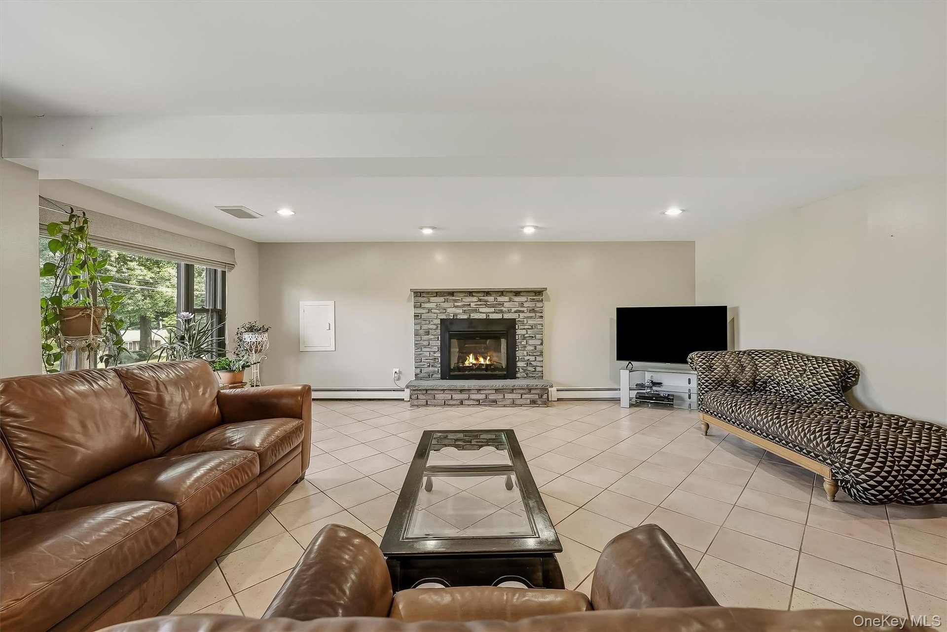 Stone-faced fireplace with hearth, tile flooring, recessed lighting, and large windows