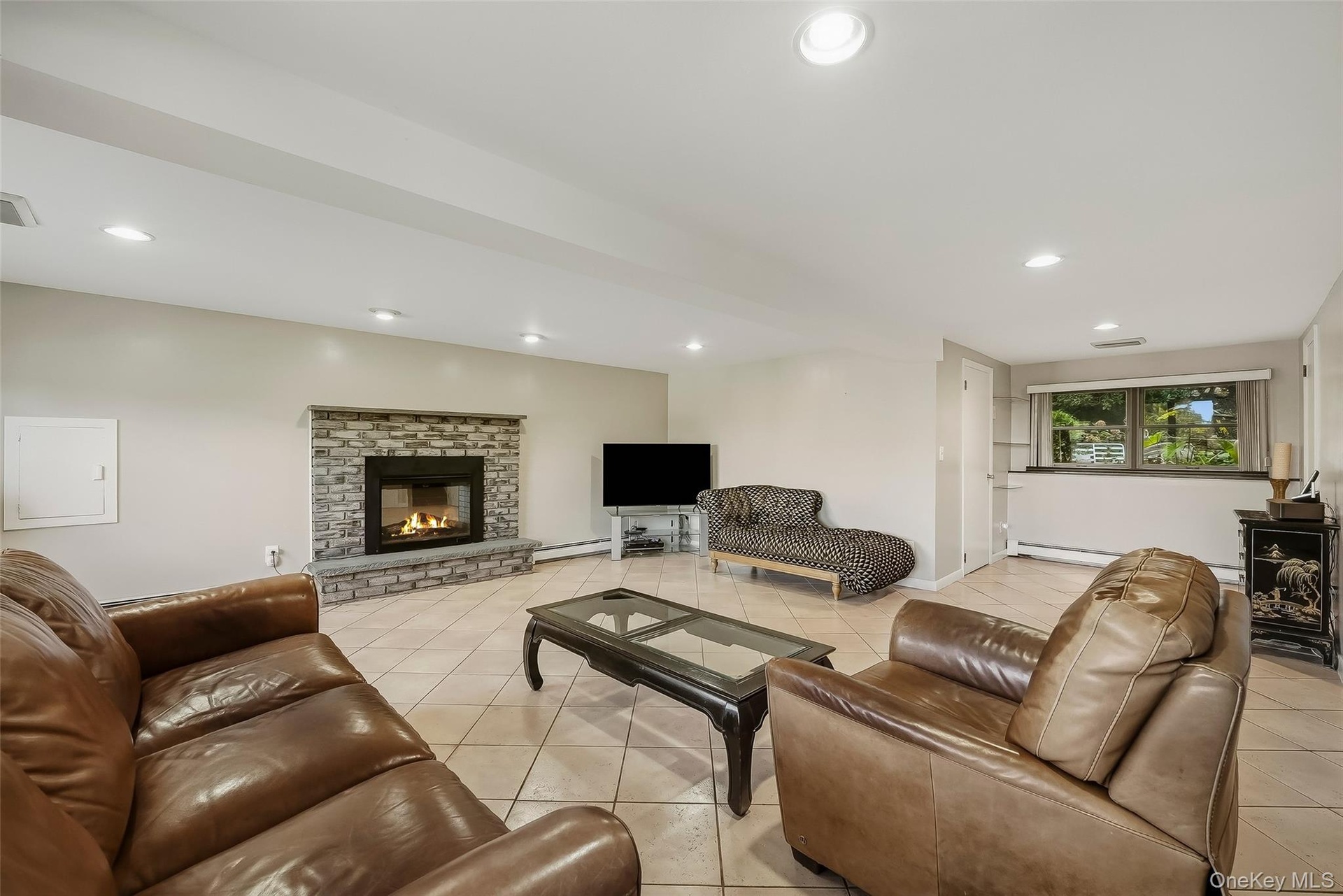 Tile flooring, stone-faced fireplace with hearth, recessed lighting, and window overlooking the backyard.