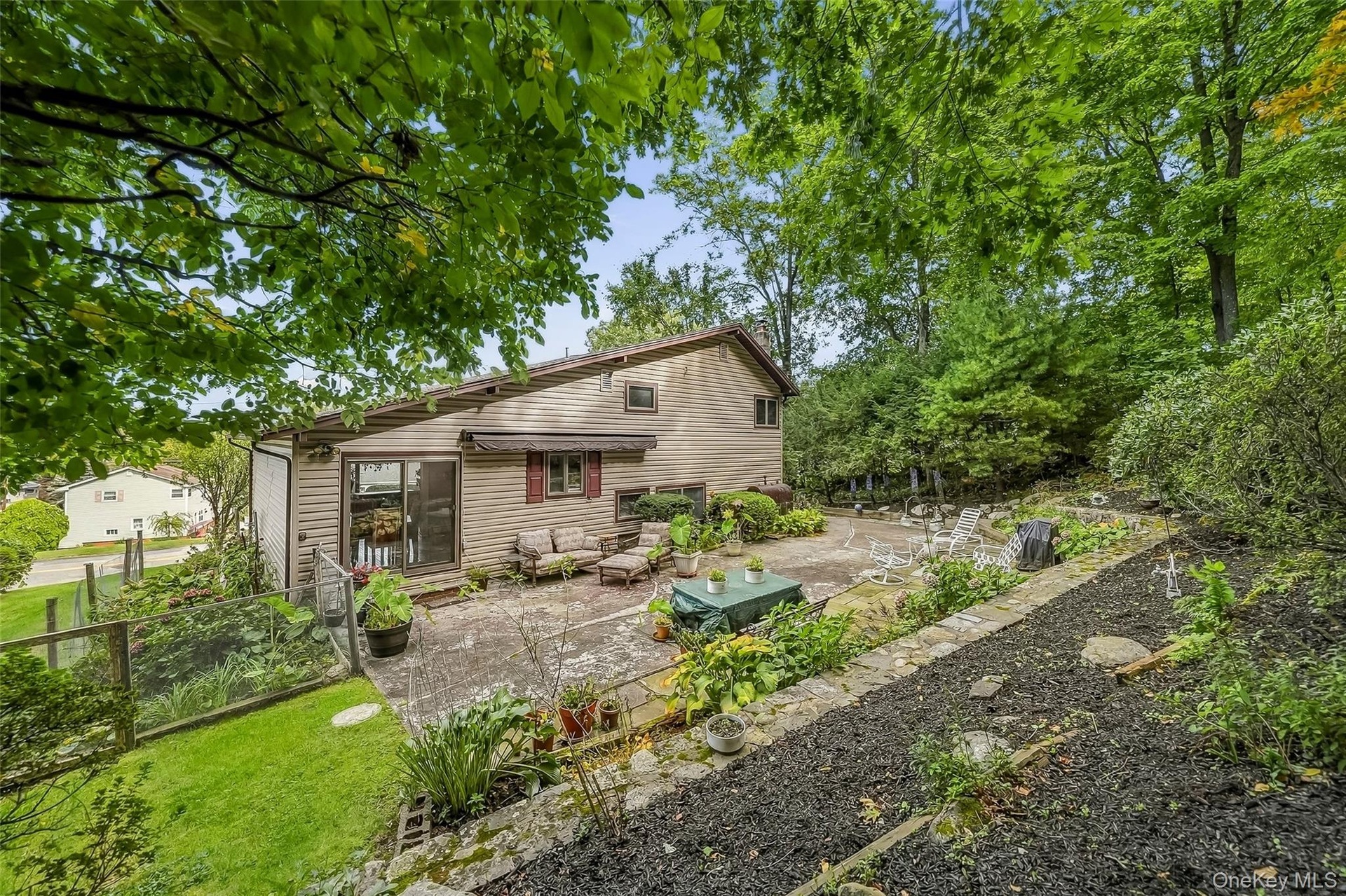 Expansive rear patio area featuring concrete paving, mature landscaping, and a tiered, mulched garden bed