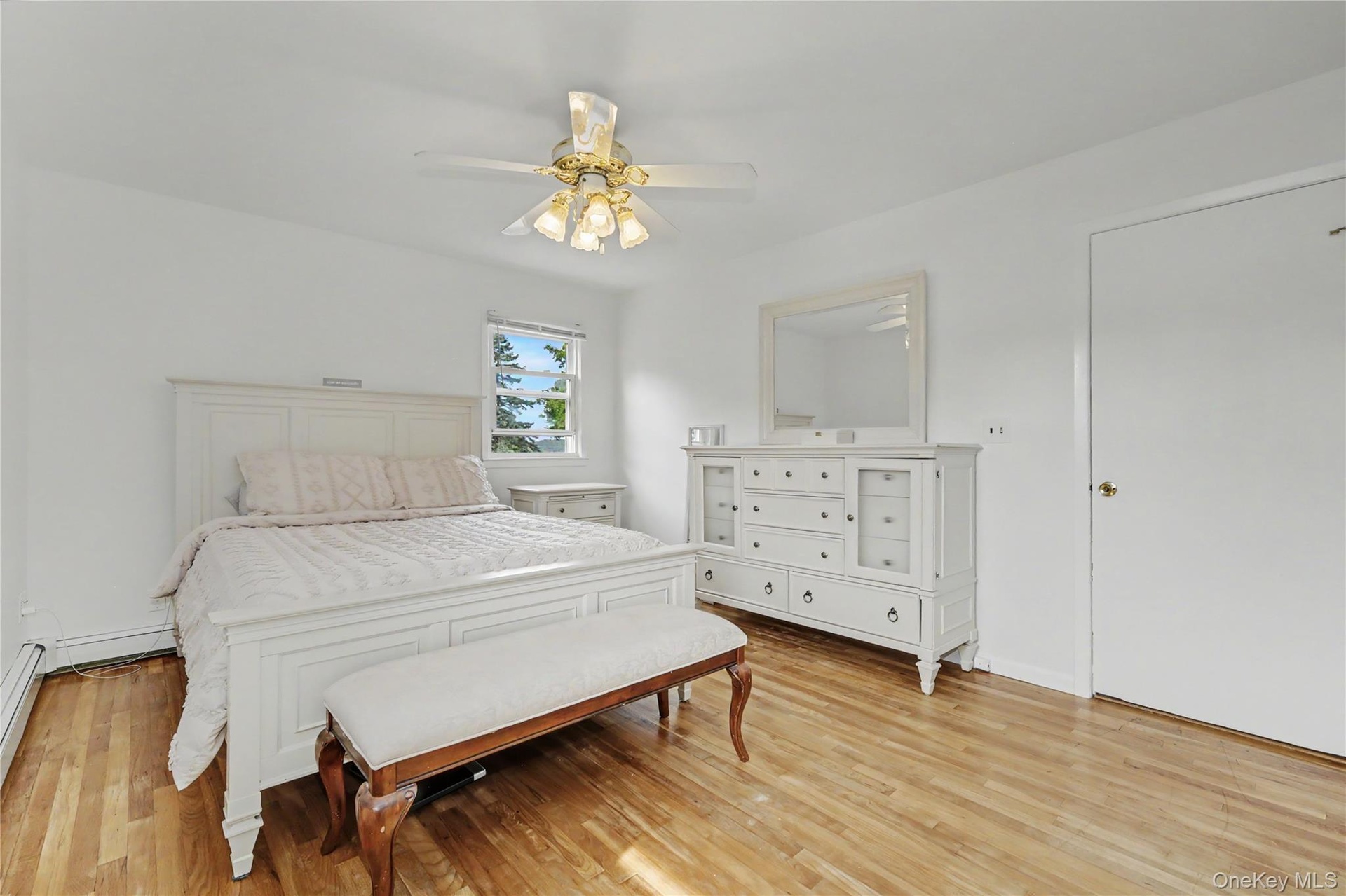 Substantially sized primary bedroom with warm oak flooring and ceiling fan
