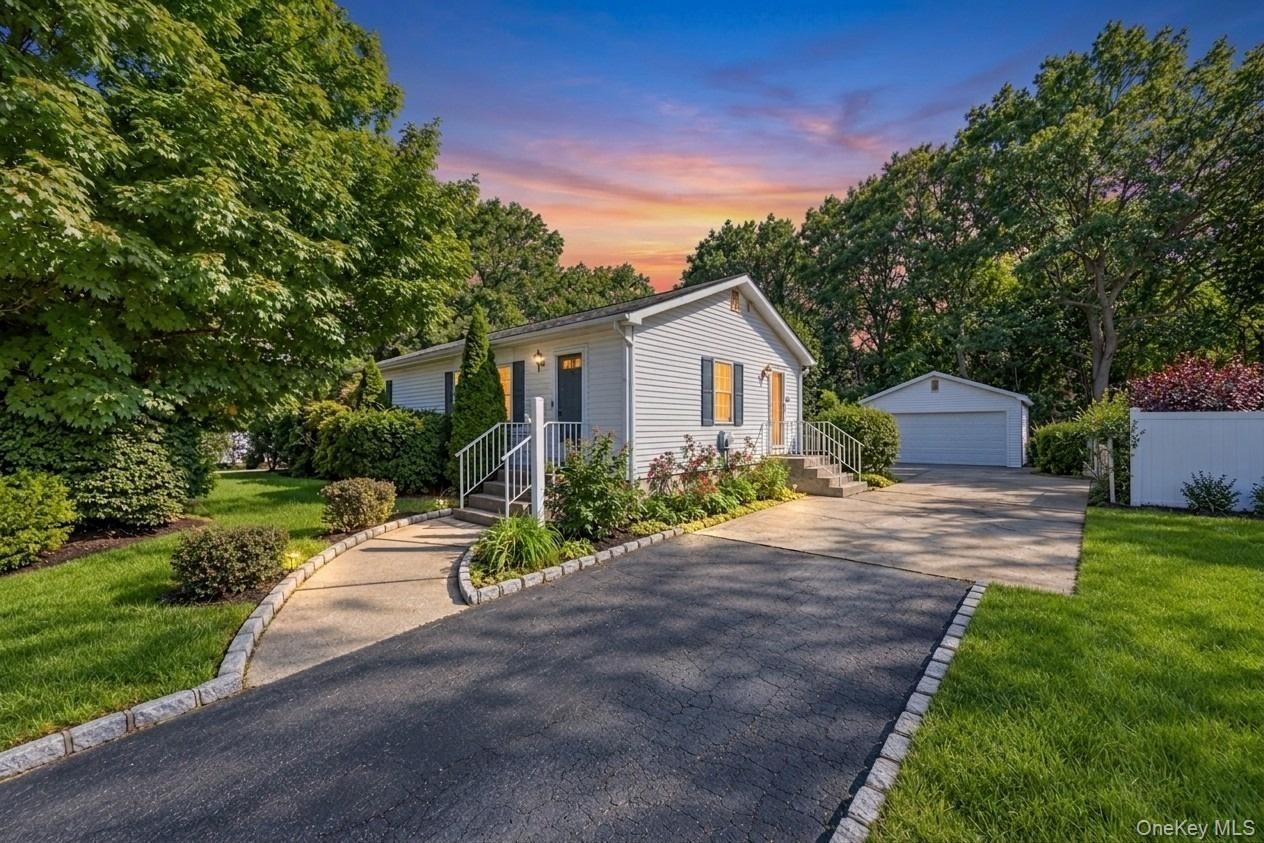Exterior featuring siding, mature trees, a paved driveway, and a detached garage