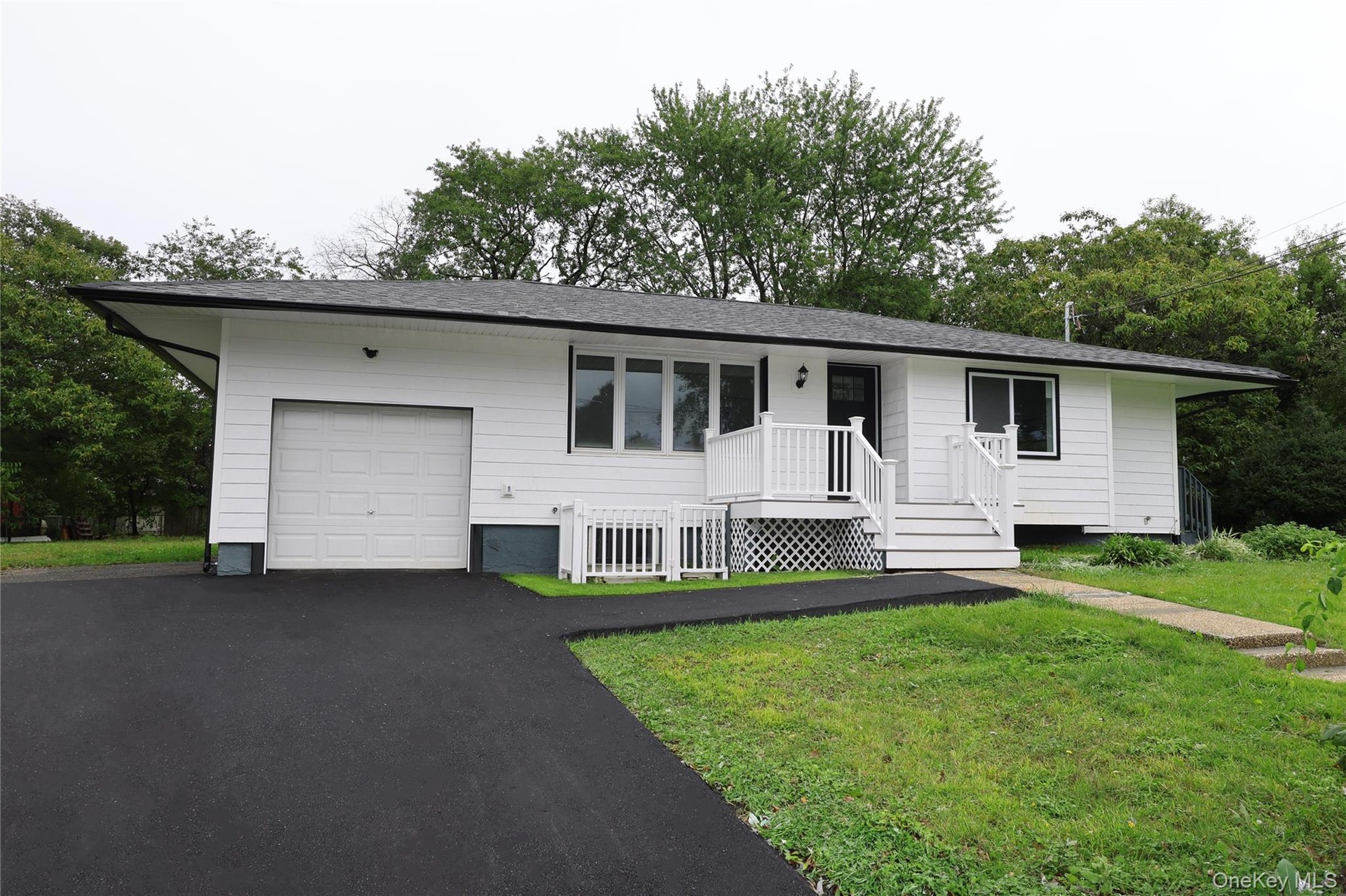 White exterior siding with dark trim, attached garage, front porch with white railing, paved driveway, and grass lawn