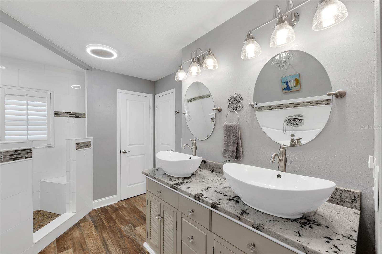 The primary bathroom has a large corner shower with multiple showerheads and built-in bench, dual sinks, linen closet storage and private water closet