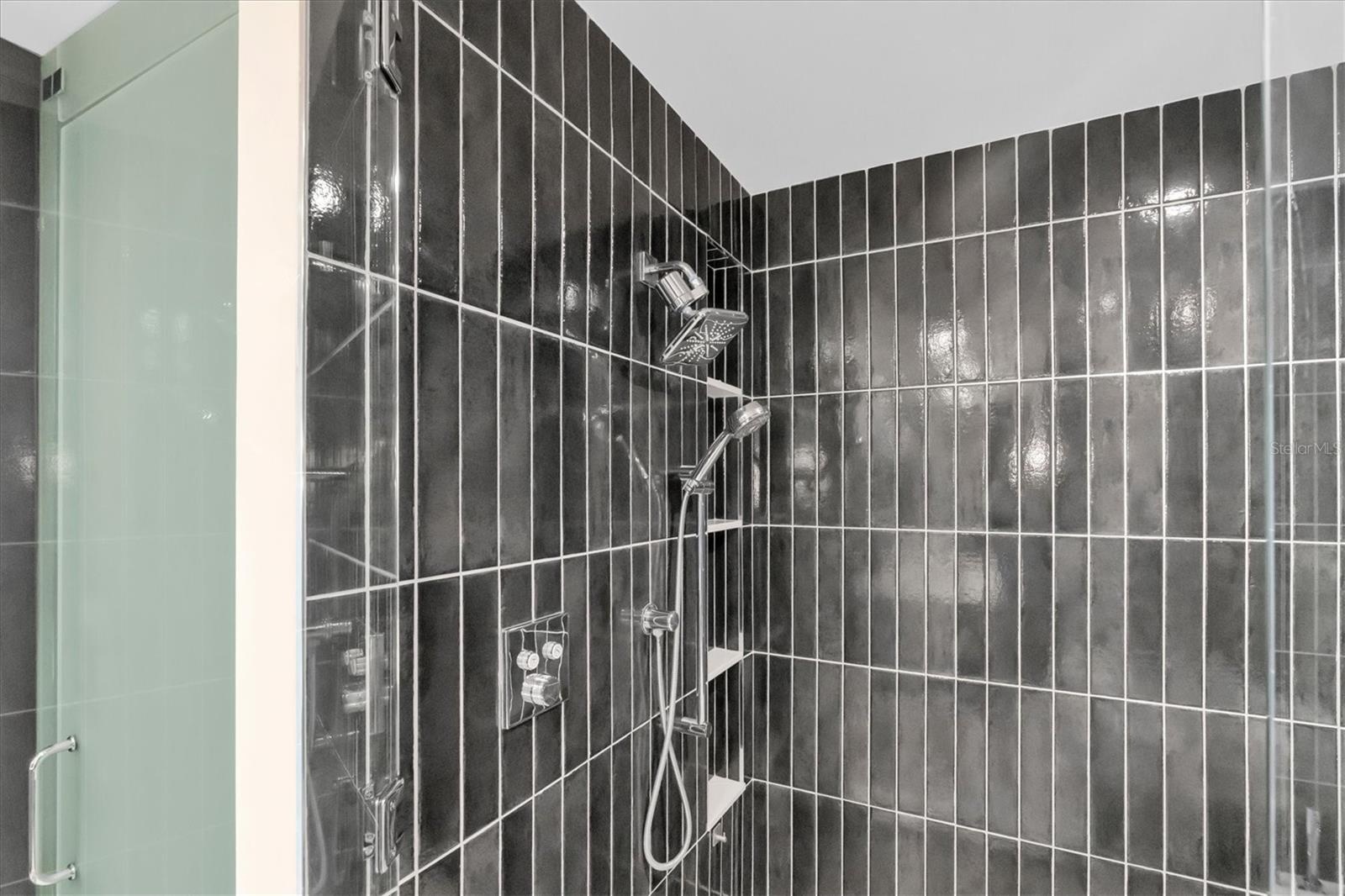 Frameless glass shower with rain fixture and dual shower heads.