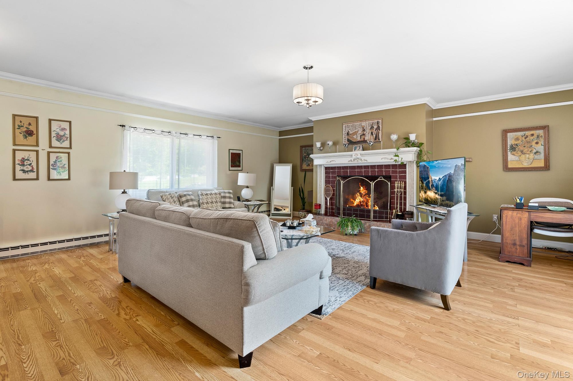 Living area with a baseboard heating unit, light wood-style floors, ornamental molding, a fireplace, and baseboards