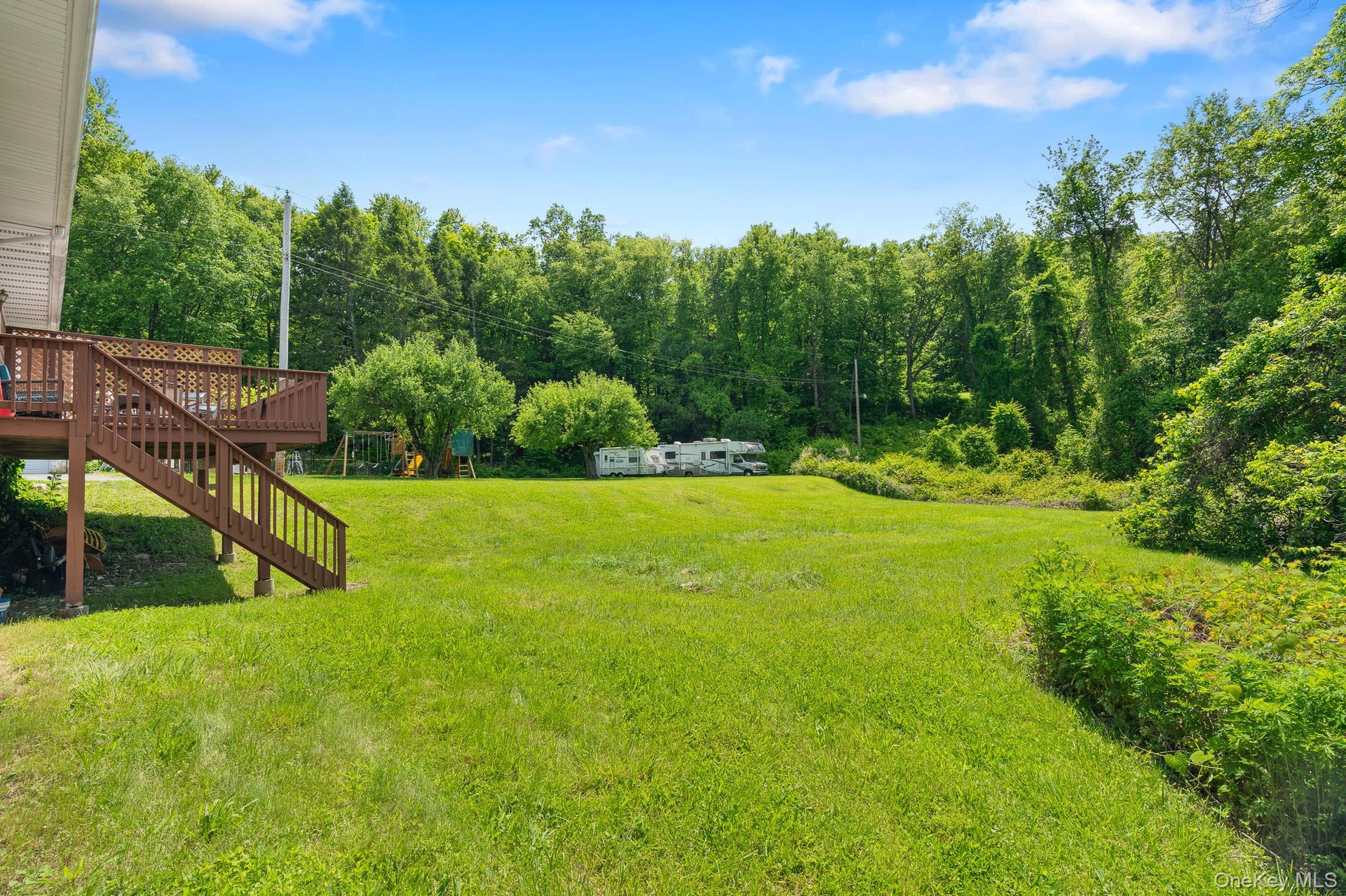 View of grassy yard featuring a deck, stairway, and a wooded view