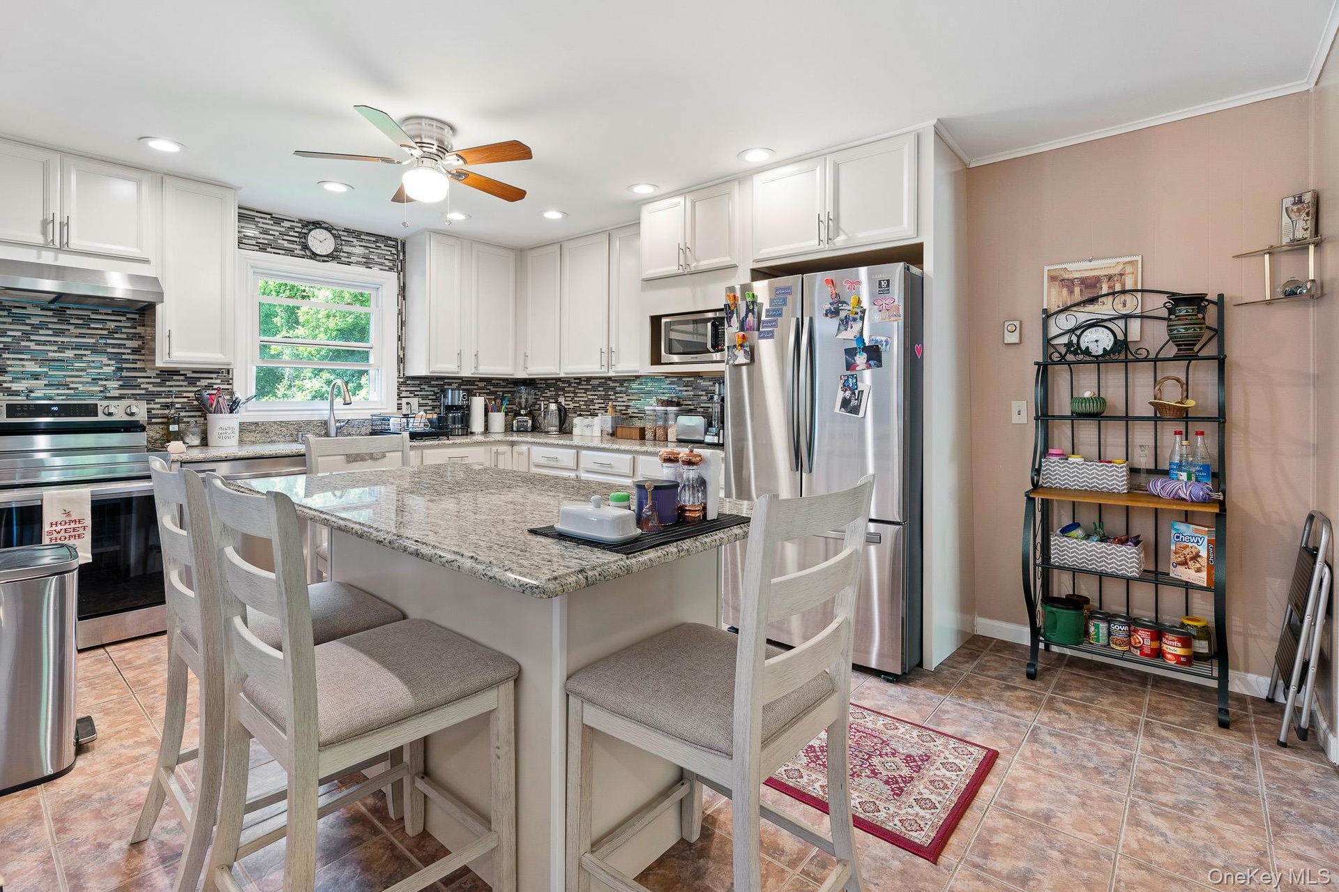 Kitchen featuring appliances with stainless steel finishes, under cabinet range hood, ceiling fan, tasteful backsplash, and a breakfast bar area
