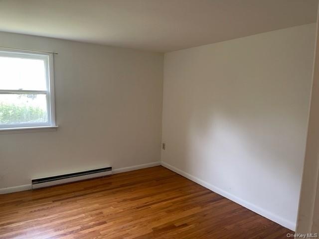 Spare room featuring a baseboard heating unit, wood finished floors, and baseboards