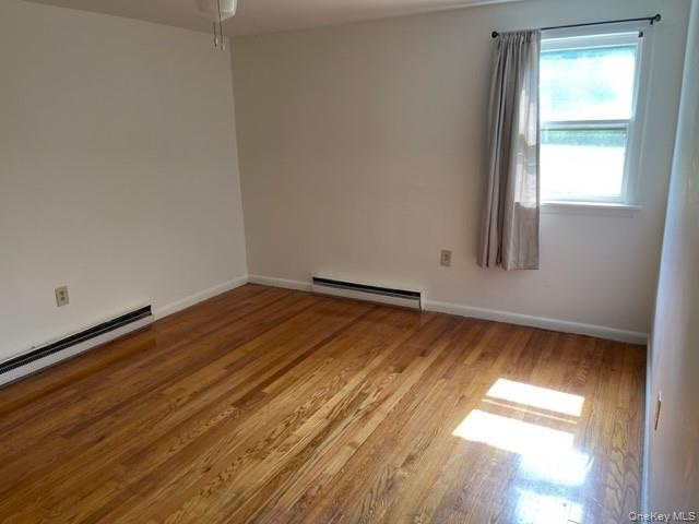 Empty room with a baseboard heating unit, wood finished floors, baseboards, and a ceiling fan
