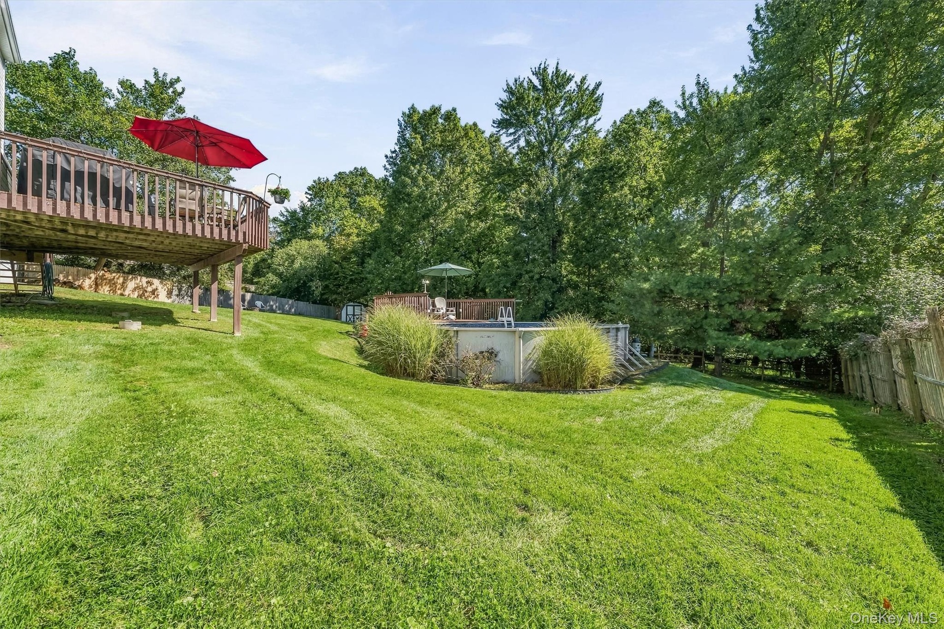 Elevated wood deck, expansive green lawn, above-ground pool, pool deck, and mature trees