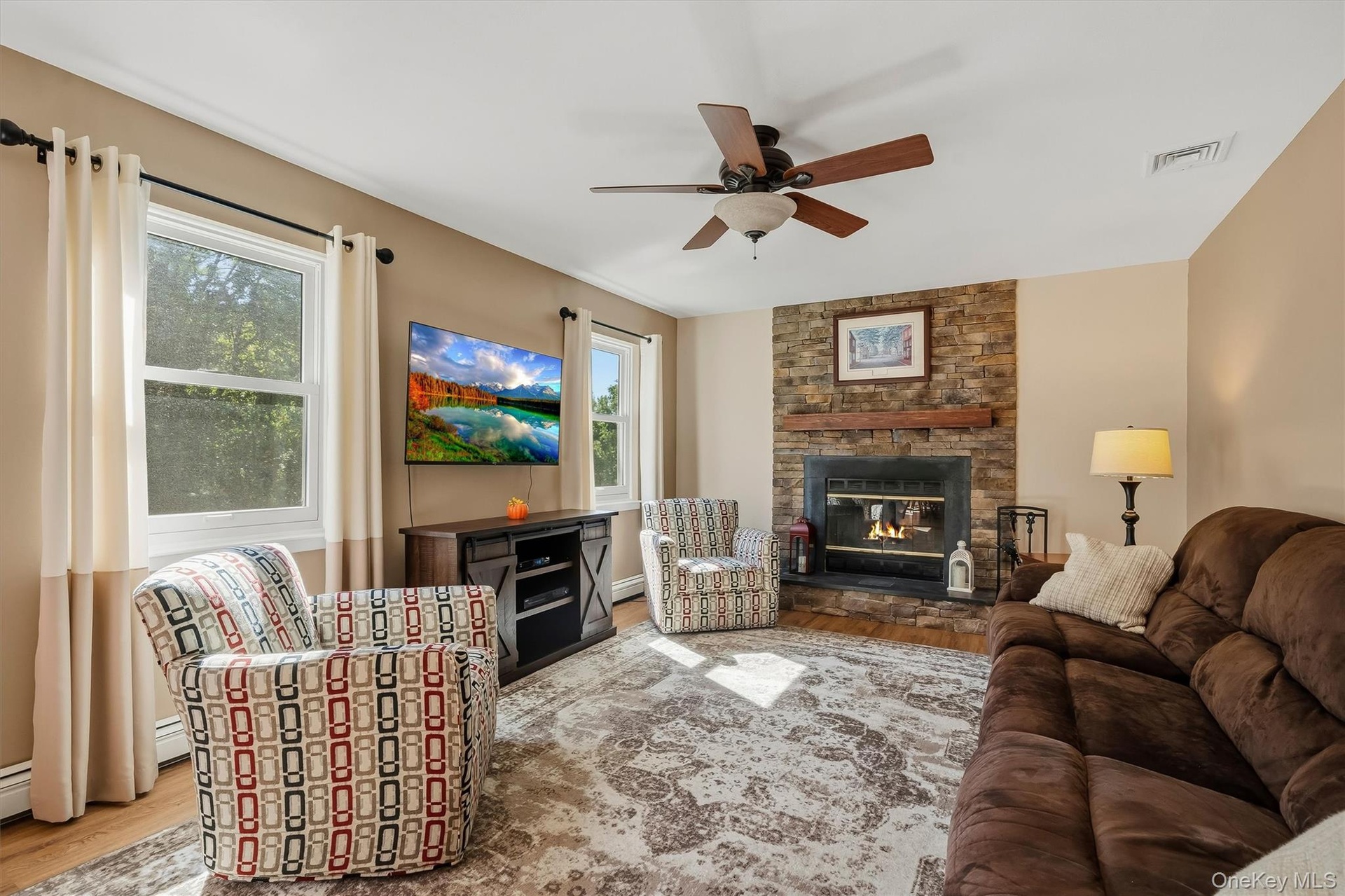 Stone-faced fireplace with a wood mantel, wood-finish flooring, and a ceiling fan