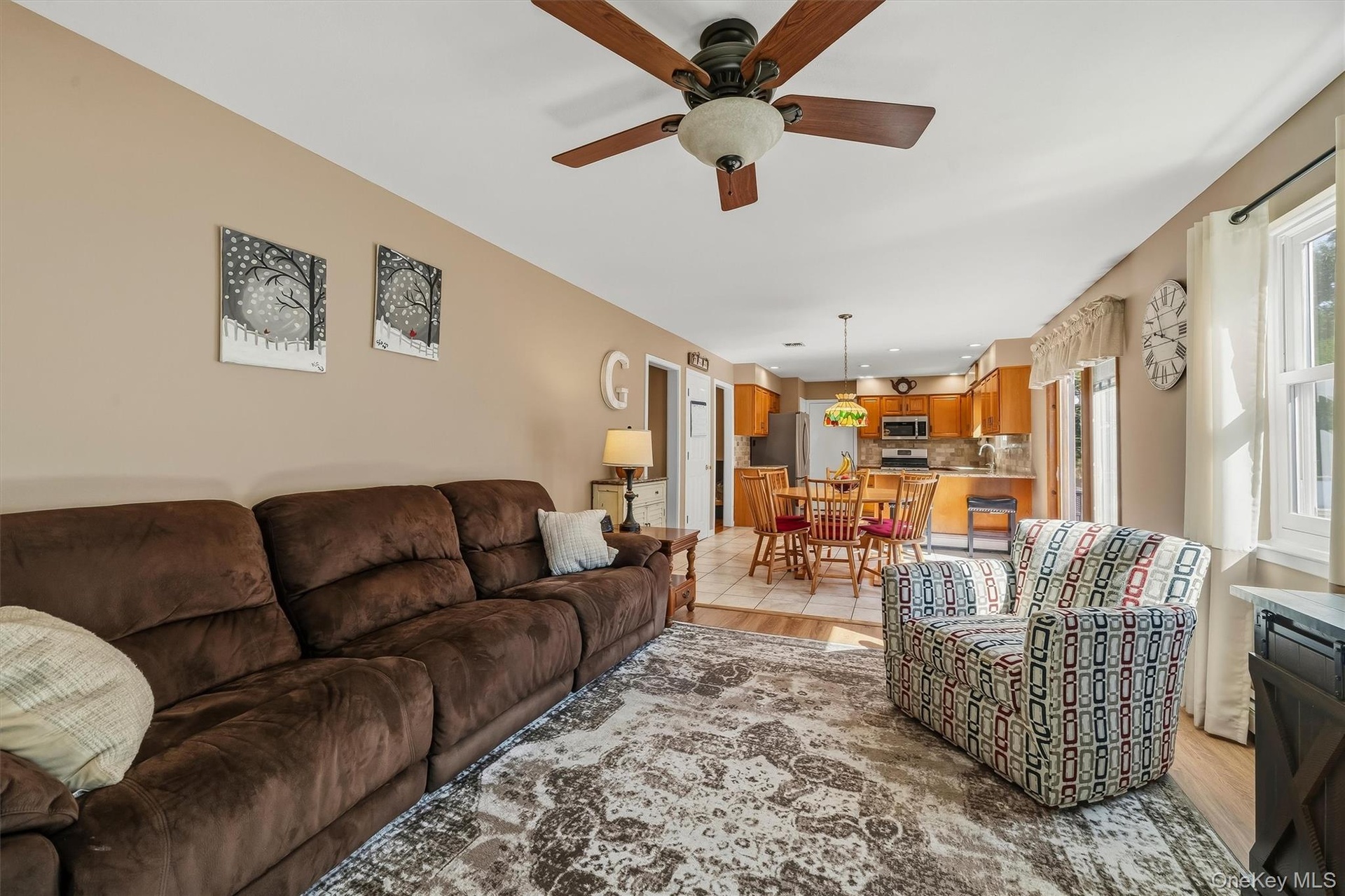 Spacious living area with ceiling fan and wood-finish flooring extending into the kitchen