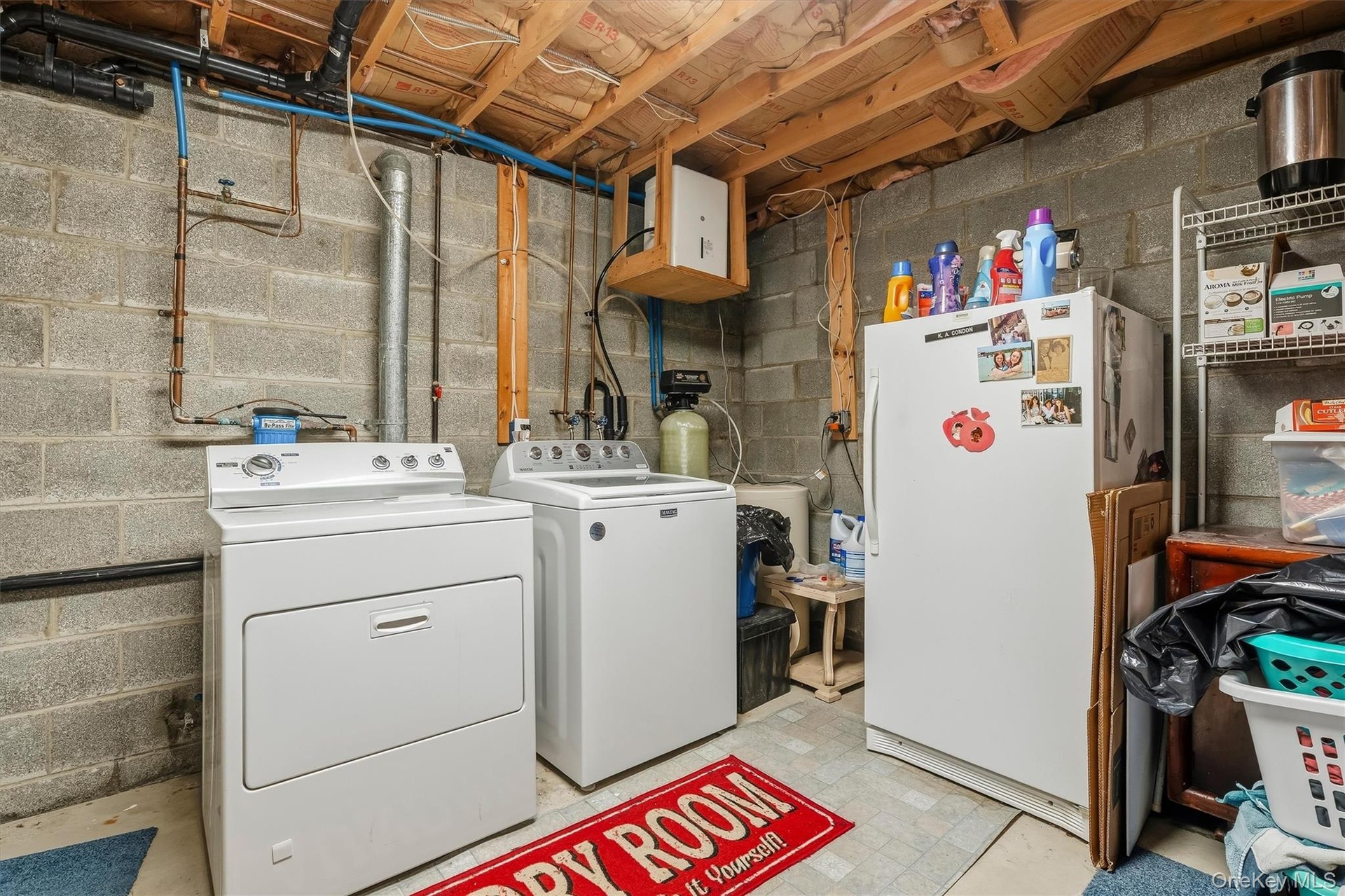 Dedicated utility area featuring a washer and dryer set, exposed ceiling joists, concrete block walls, and visible plumbing