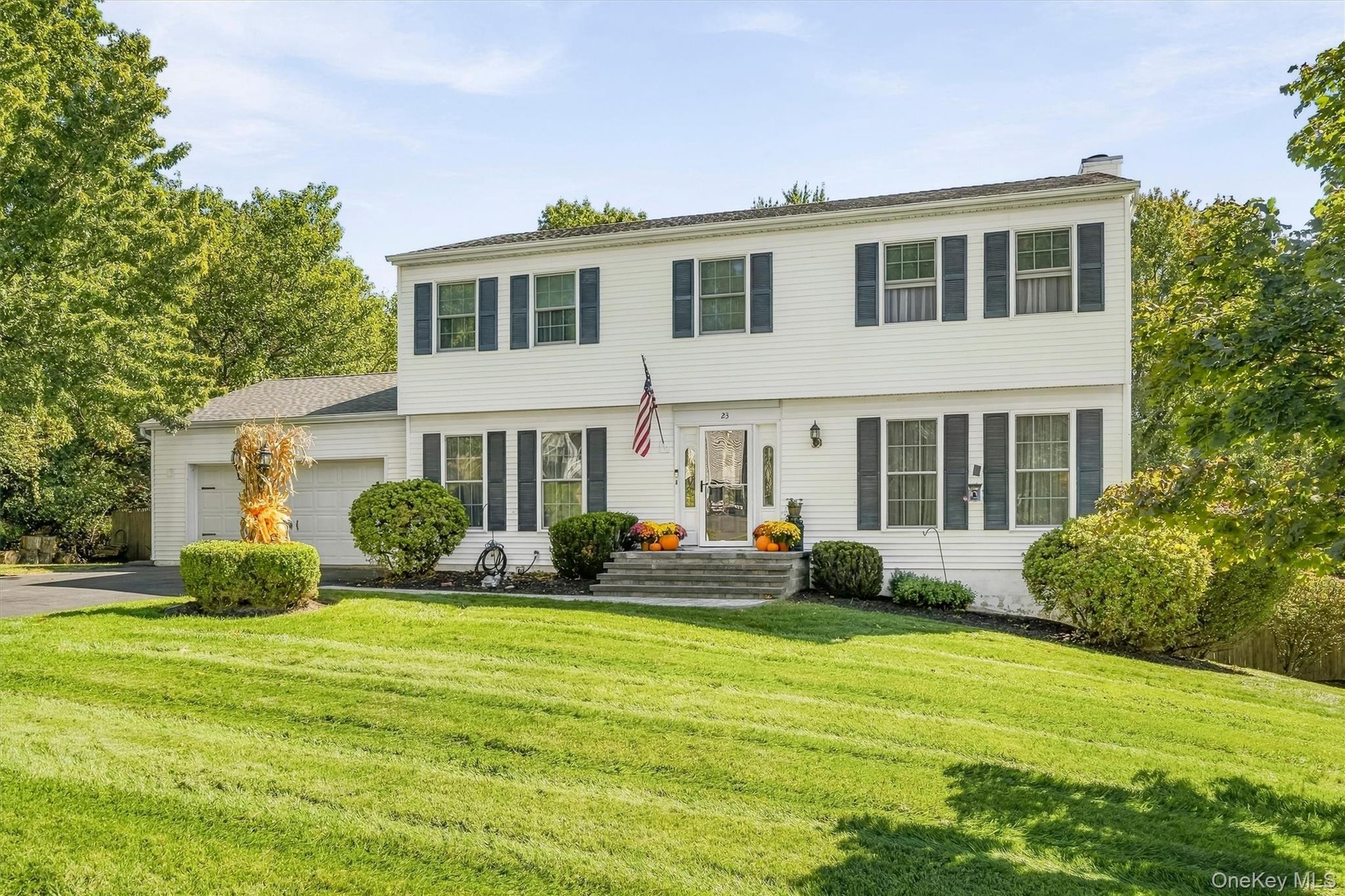 White siding exterior with dark shutters, attached two-car garage, established front landscaping, and a paved driveway
