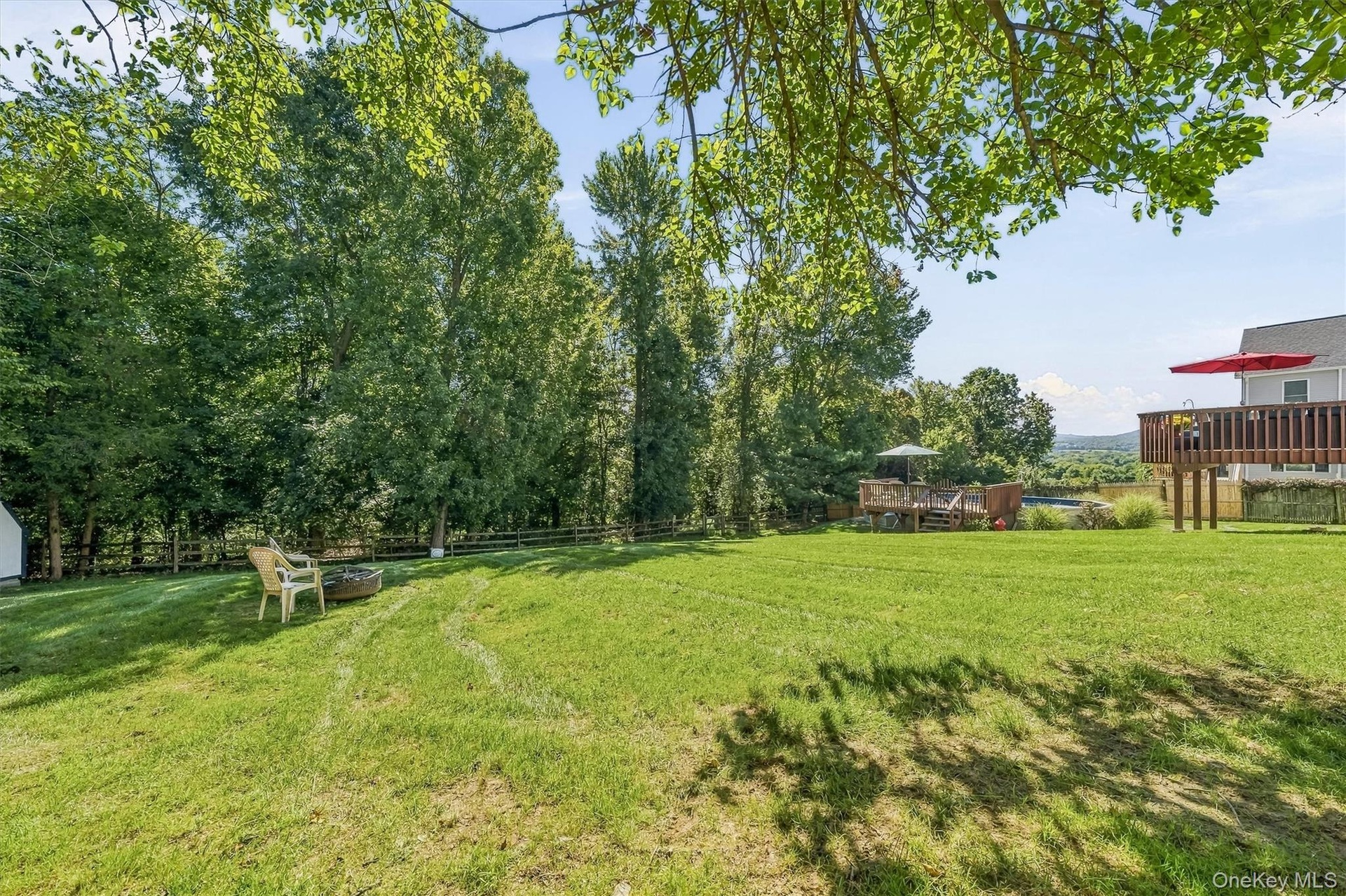 Expansive lawn area with mature trees, a fire pit, and a multi-level wooden deck
