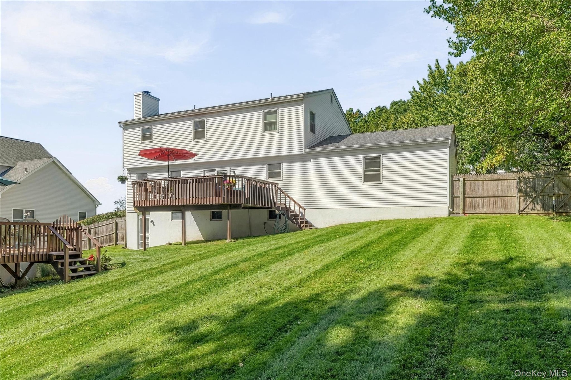 Expansive green lawn with a wood fence, two-story structure with siding, and a large wood deck with stairs