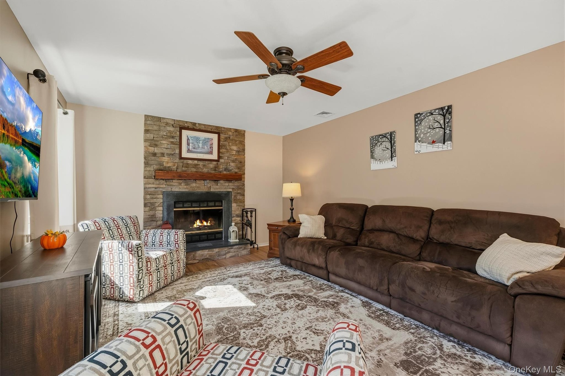Stone-surround fireplace with a wood mantle, ceiling fan with integrated lighting, recessed lighting, and warm neutral wall tones