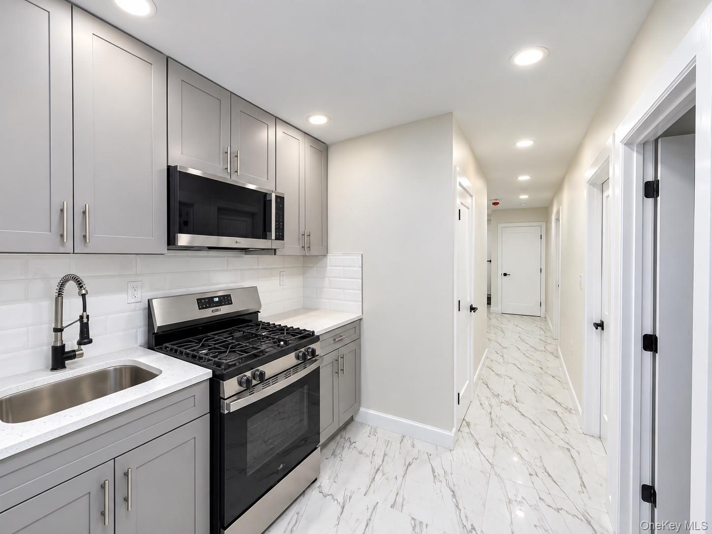 Kitchen featuring stainless steel appliances, grey cabinetry, white countertop, and subway tile backsplash