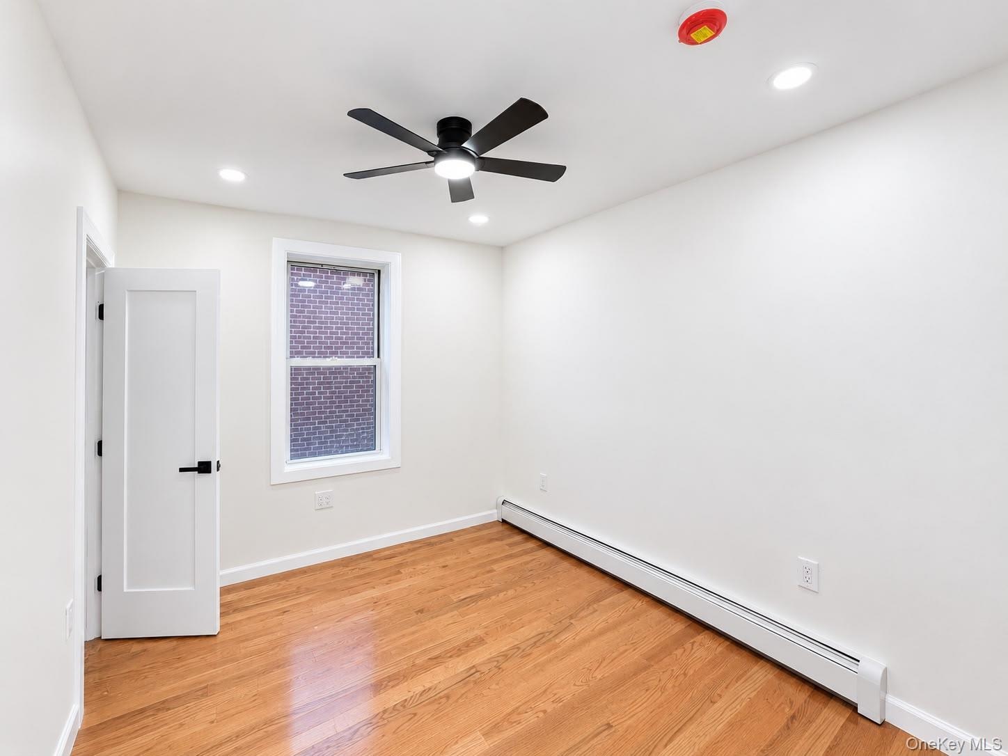 Hardwood flooring, recessed lighting, modern ceiling fan, white paneled door with matte black hardware, and baseboard heating