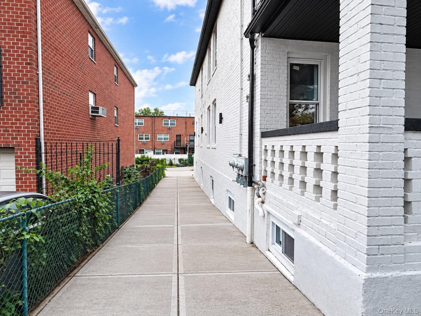 Concrete walkway with a chain-link fence, brick exterior, and a porch with a decorative railing