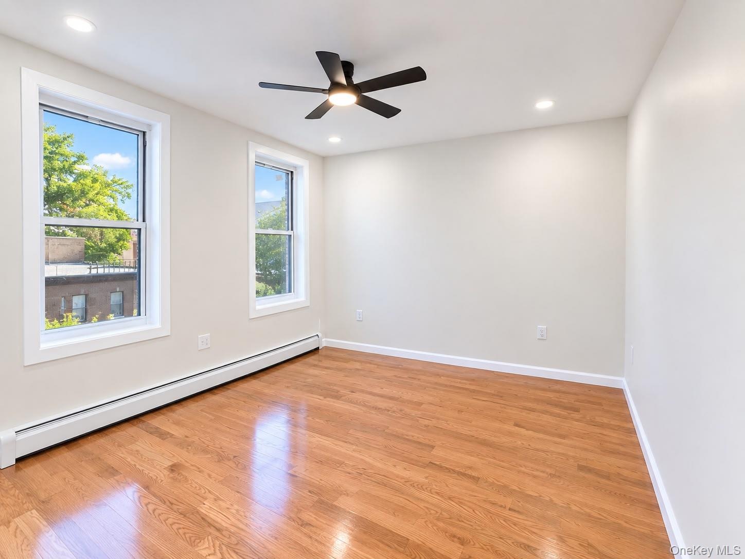 Polished wood-finish flooring, two large windows, recessed lighting, and a ceiling fan with integrated lighting