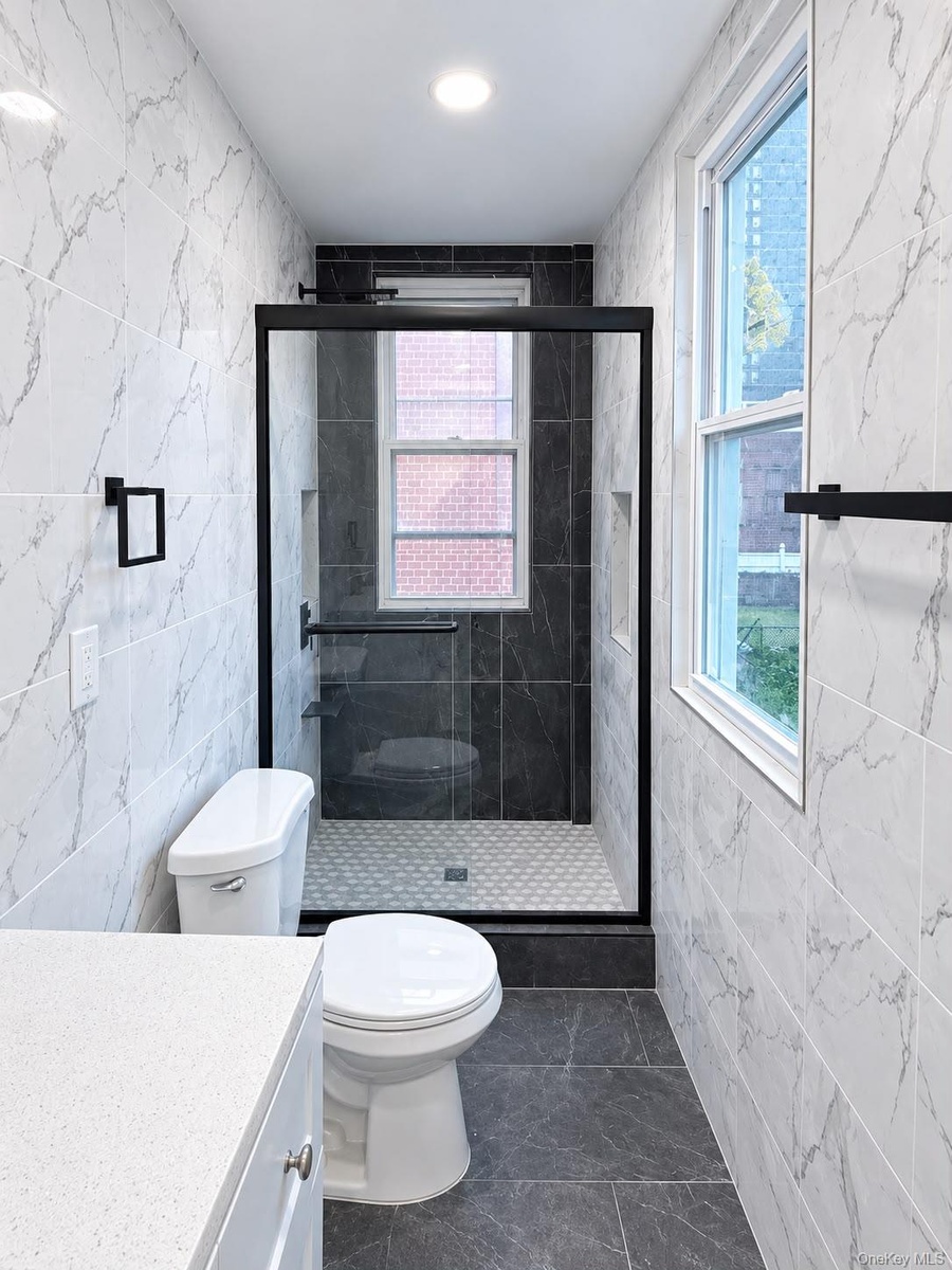 Walk-in shower with dark tile surround, built-in shelving, and black-framed glass enclosure
