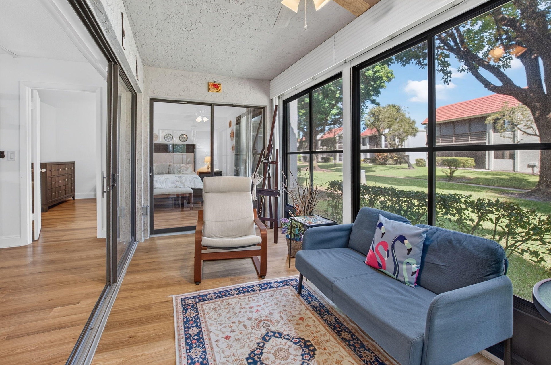 Enclosed Florida room with wood-finish flooring, ceiling fan, and large windows with lush garden views