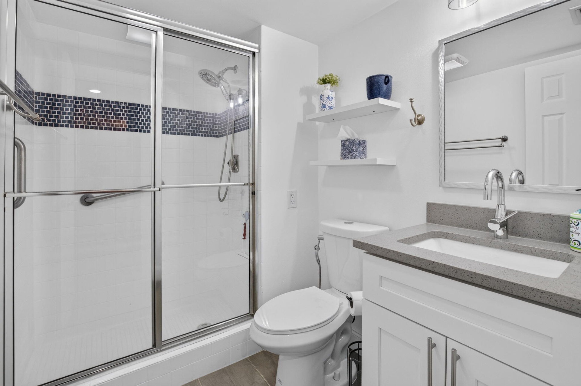 Walk-in shower with sliding glass doors, white tiled walls, and a decorative mosaic accent band