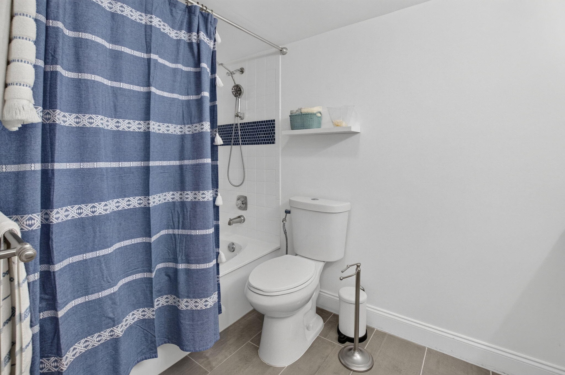 Bathtub with subway tile surround and mosaic accent, white toilet, and tile flooring