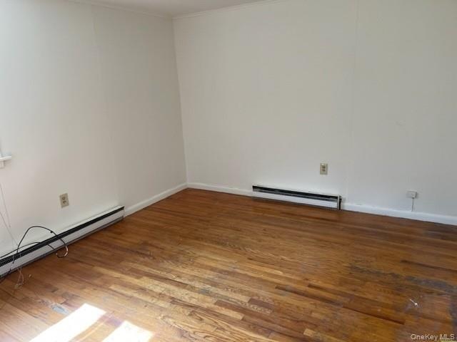 Spare room with baseboard heating, a baseboard heating unit, wood finished floors, baseboards, and ornamental molding
