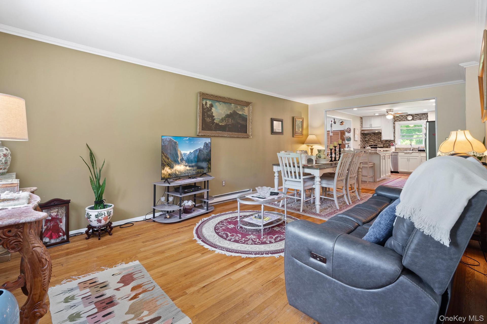 Living area with light wood-style floors, crown molding, baseboards, ceiling fan, and a baseboard radiator