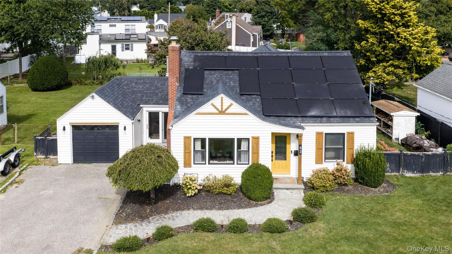 White siding exterior with a dark shingled roof, featuring solar panels and a brick chimney