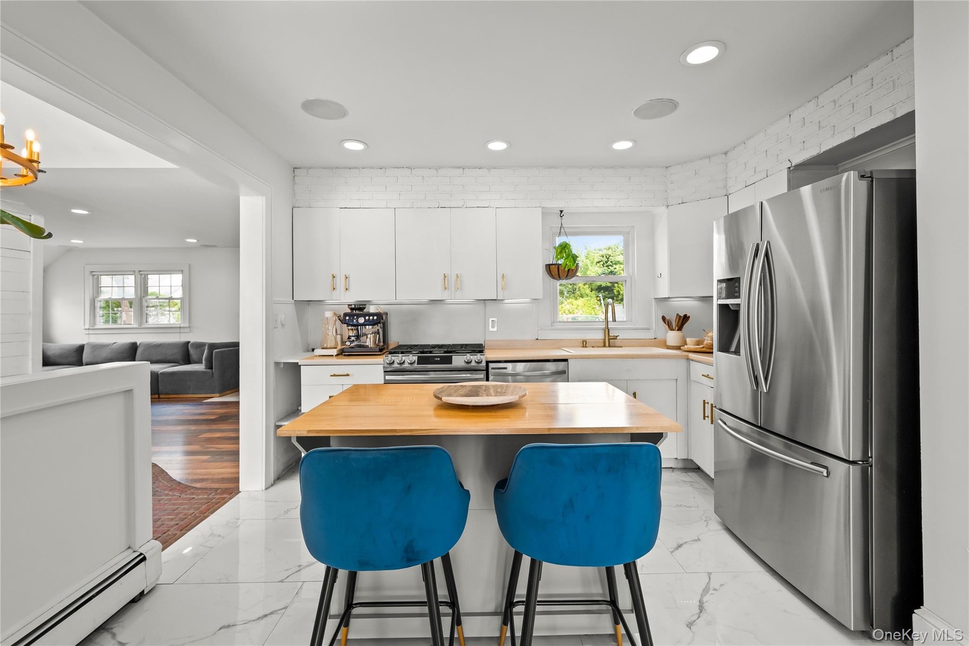 Modern kitchen featuring white cabinetry, stainless steel appliances, wood-finish countertops, recessed lighting, and large format tile flooring