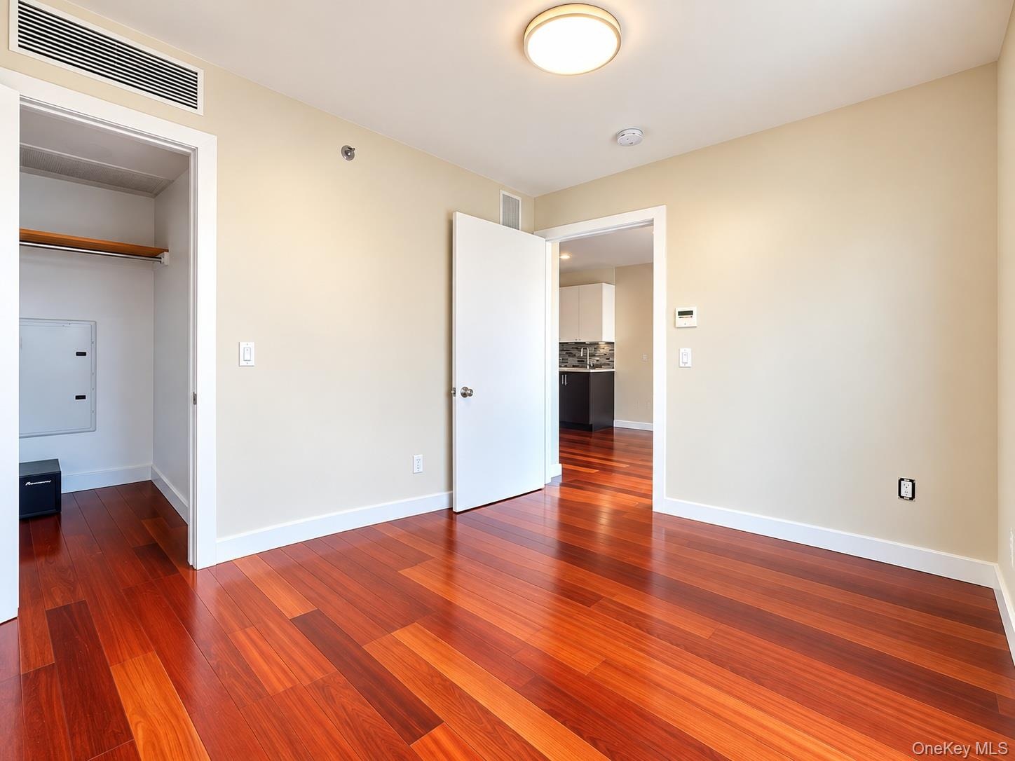 Hardwood-style flooring throughout, featuring a built-in closet with a clothes rod, light-toned walls, and a flush-mount ceiling light