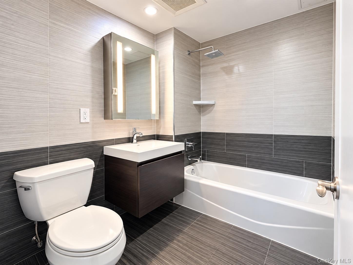 Modern bathroom featuring a floating vanity with integrated sink, illuminated medicine cabinet, rainfall shower head, and two-tone tile walls