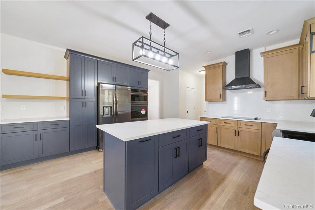 Kitchen featuring wall chimney exhaust hood, light wood-type flooring, pendant lighting, a kitchen island, and black appliances
