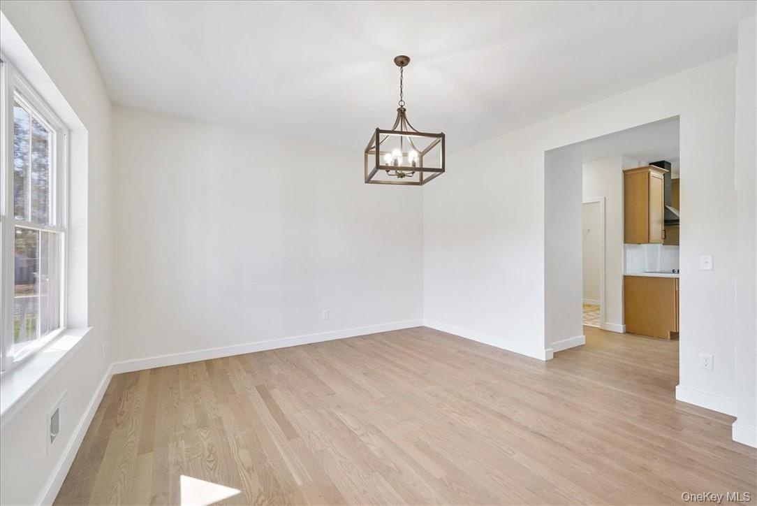 Unfurnished room featuring plenty of natural light, a notable chandelier, and light wood-type flooring