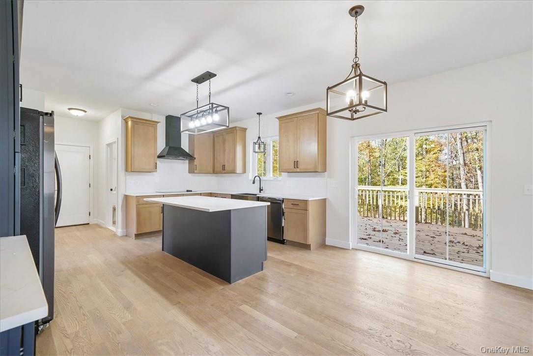 Kitchen featuring appliances with stainless steel finishes, hanging light fixtures, wall chimney range hood, and a kitchen island