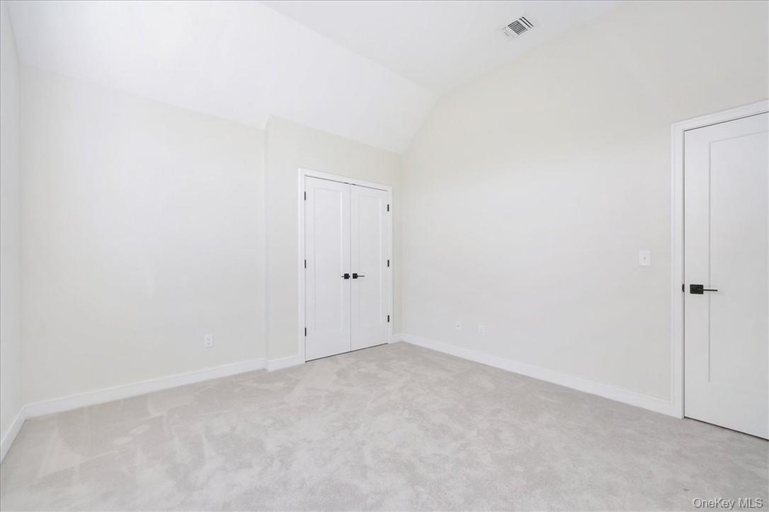 Carpeted spare room featuring vaulted ceiling