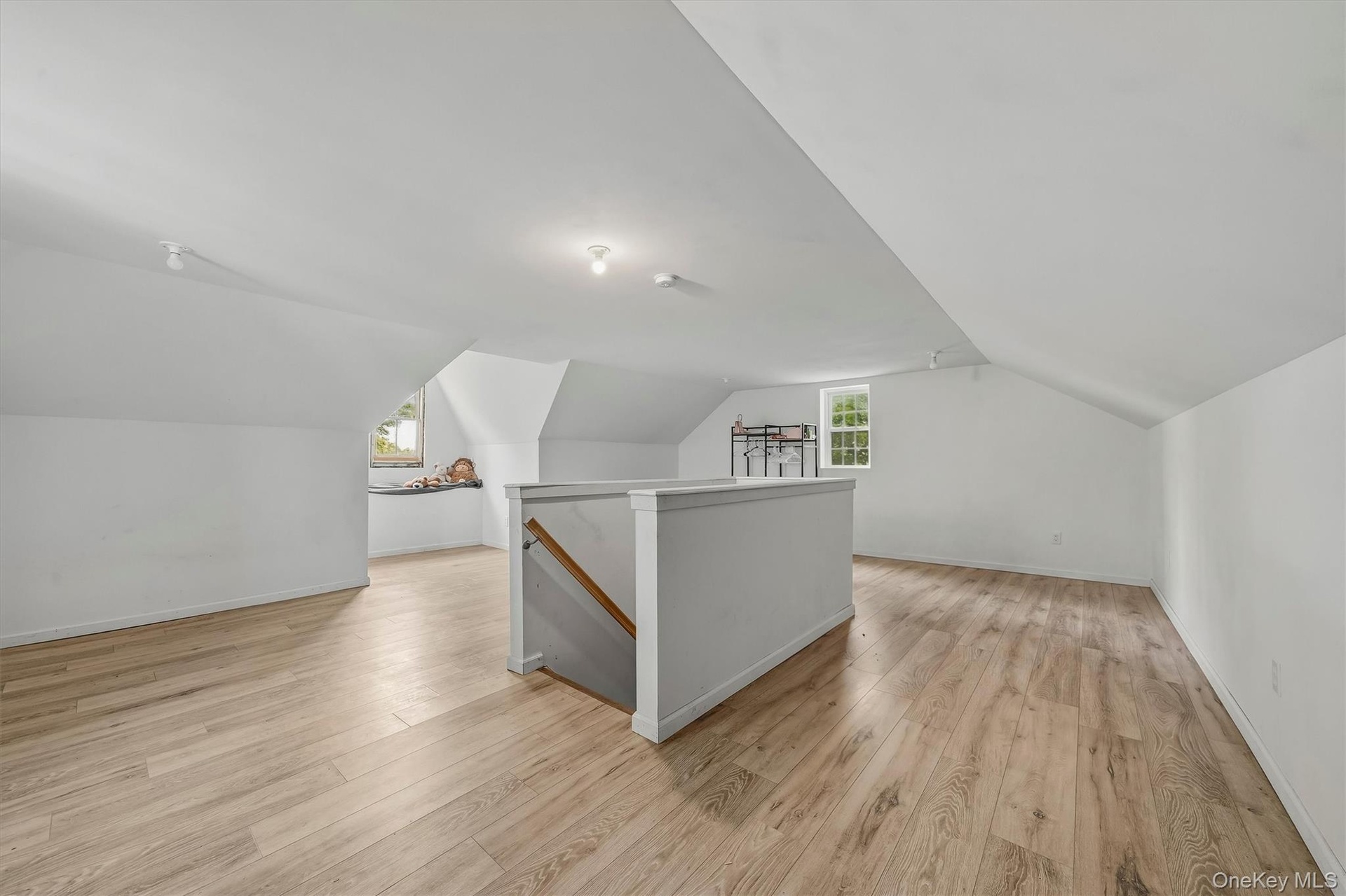 Expansive attic space featuring wood-finish flooring, sloped ceilings, multiple windows, and track lighting
