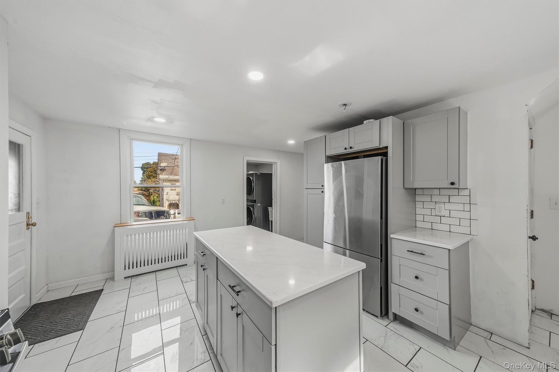 Kitchen featuring a central island with countertop, stainless steel refrigerator, light gray cabinetry, subway tile backsplash, and white tile floorin