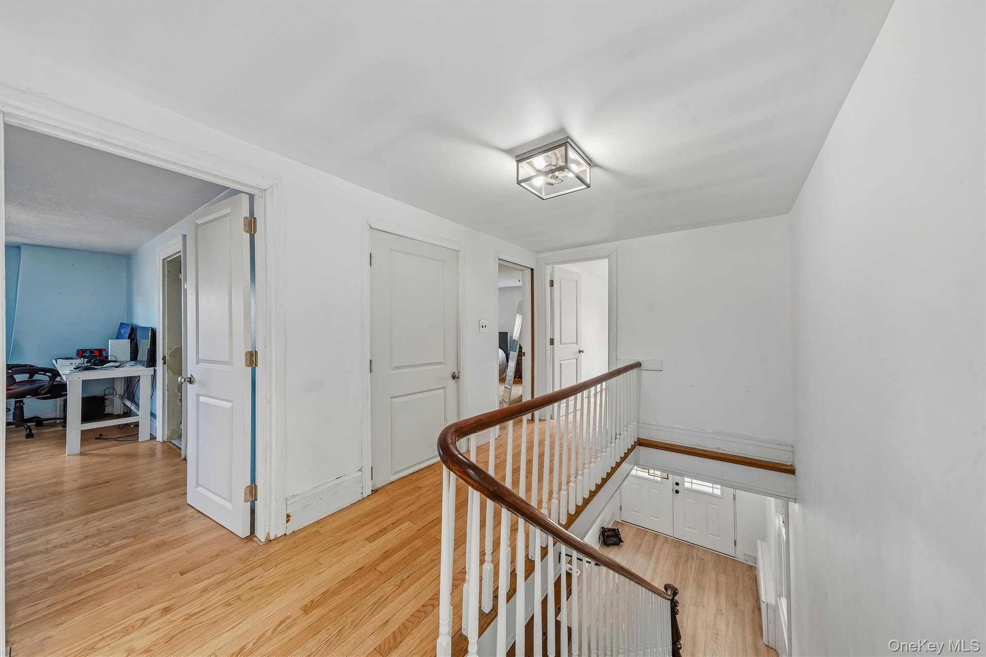 Hardwood flooring throughout, white walls, white doors, and a wood-finish handrail with white balusters