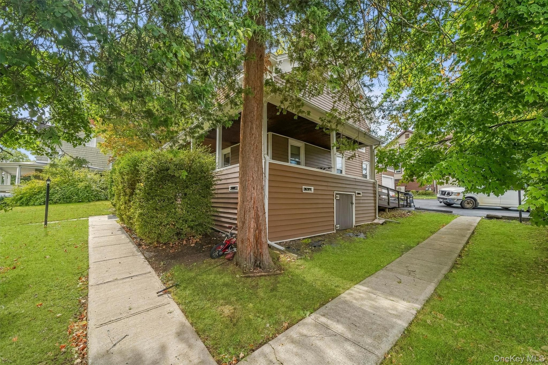 Siding exterior with a covered porch, mature trees, concrete walkways, and a ramp access point