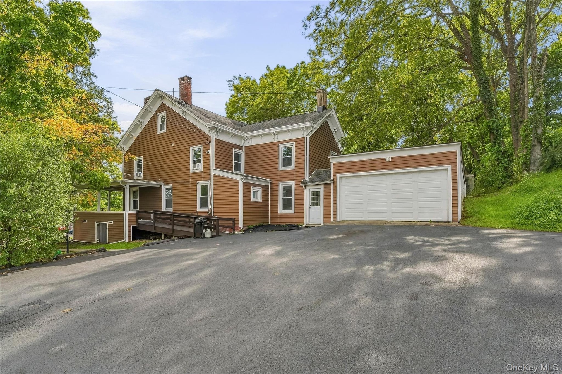 Brown siding exterior with white trim, attached garage with white door, paved driveway, covered porch, and accessible ramp entry