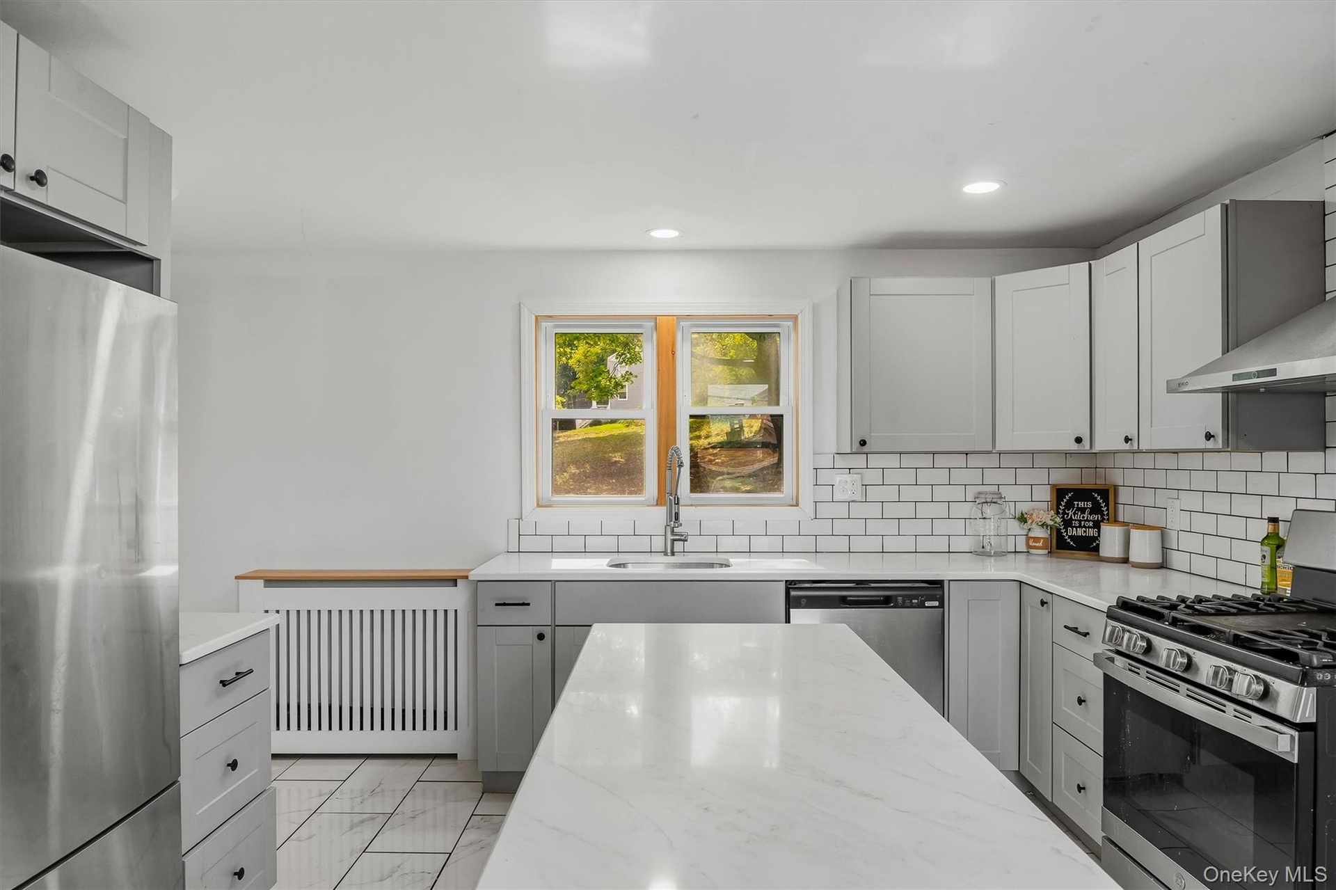 Modern kitchen with light grey cabinetry, white subway tile backsplash, stainless steel appliances, and a central island with a white countertop