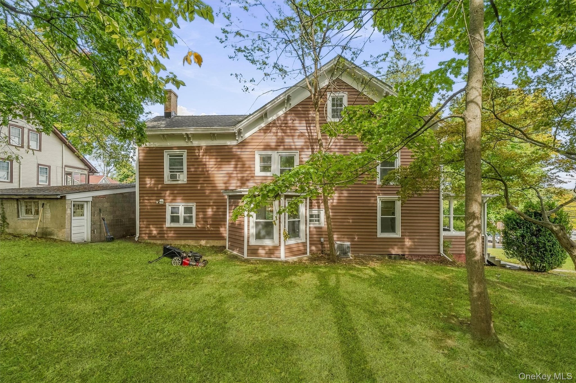 Expansive green lawn with mature trees and a brown-sided residence featuring multiple windows and a chimney